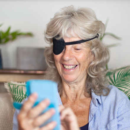 Elderly woman with eye patch smiling on phone