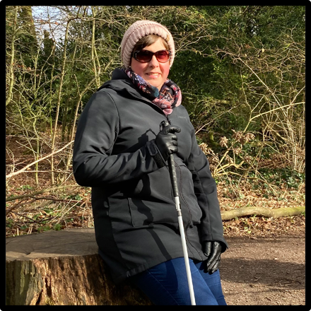 Louise smiling at the camera in  the woods holding a cane