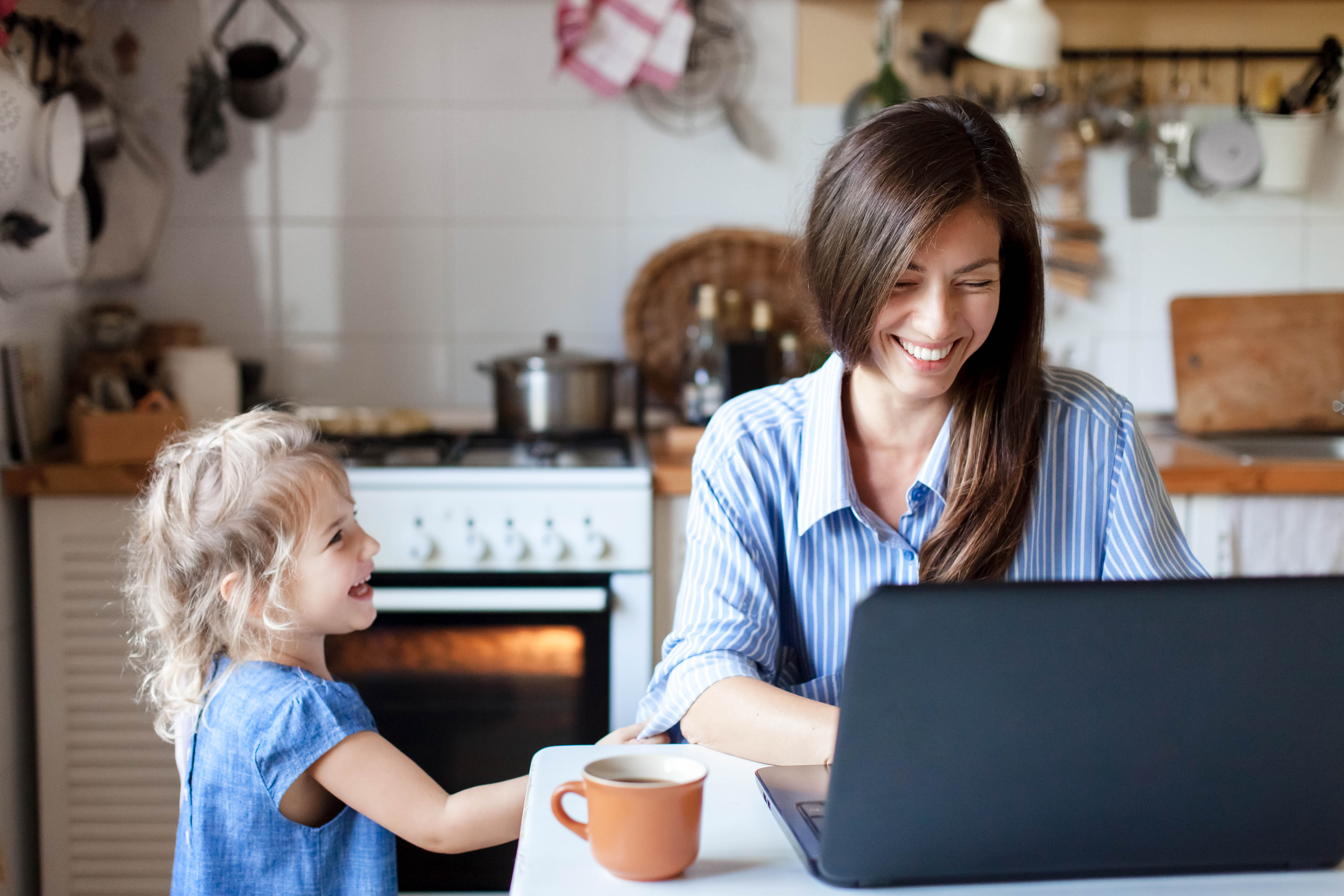 Mother and young daughter on laptop in kitchen laughing