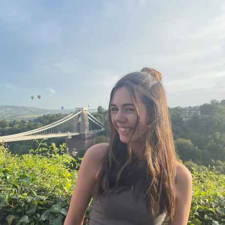 Emily, a white female in her 20s with long dark hair, smiling and posing with the Clifton Suspension Bridge in the background