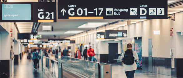 Departures at an airport. The middle of the image is a walking conveyer belt and a person walking towards it. Above are the gate numbers.