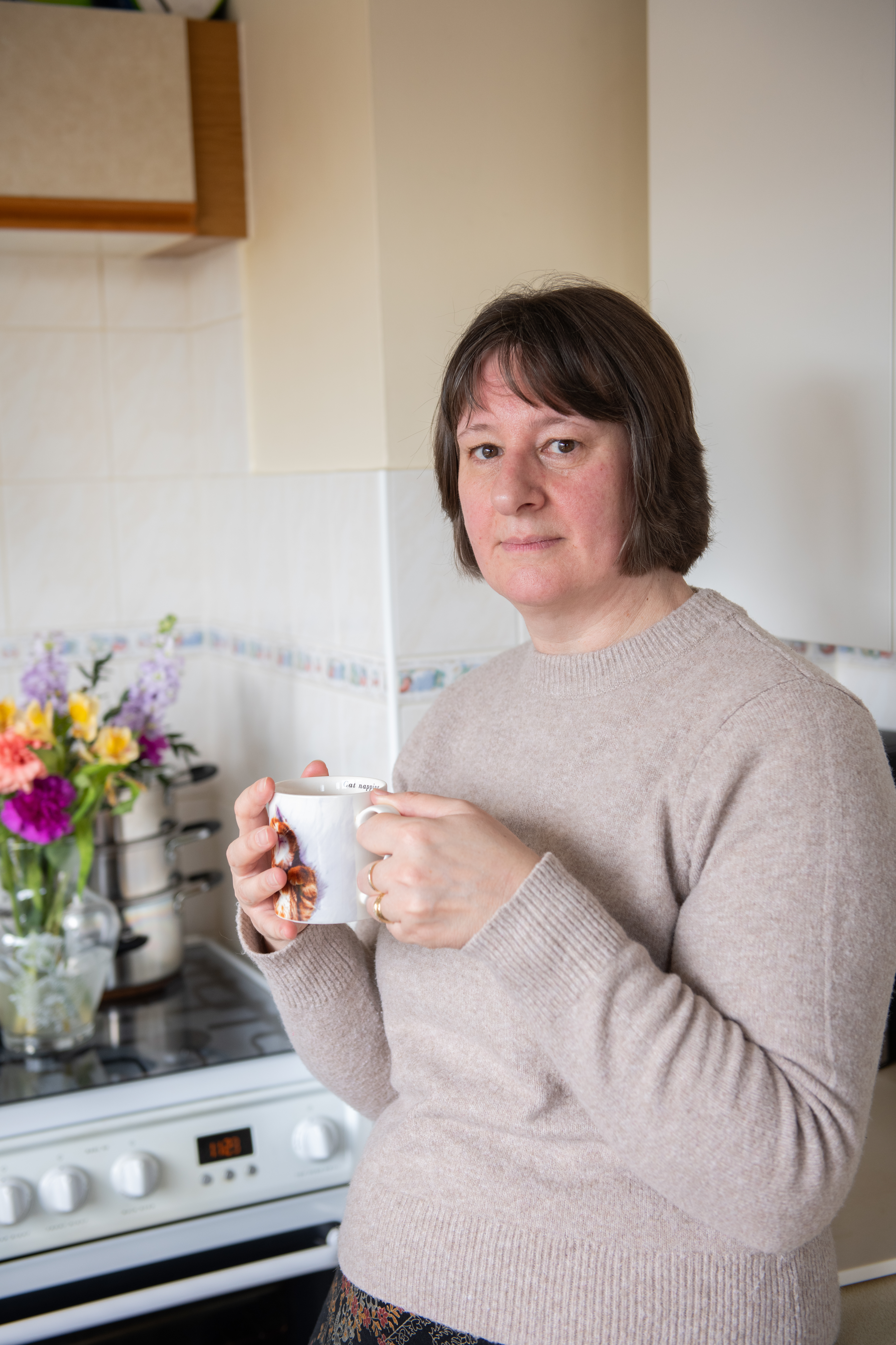 Nancy in her kitchen looking into the camera with a cup of tea