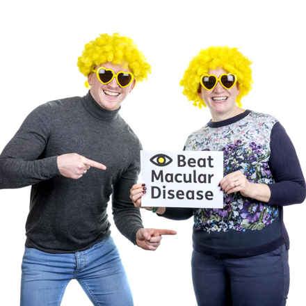 Macular Week 2022 man and woman with sign in Macular Society wigs and glasses