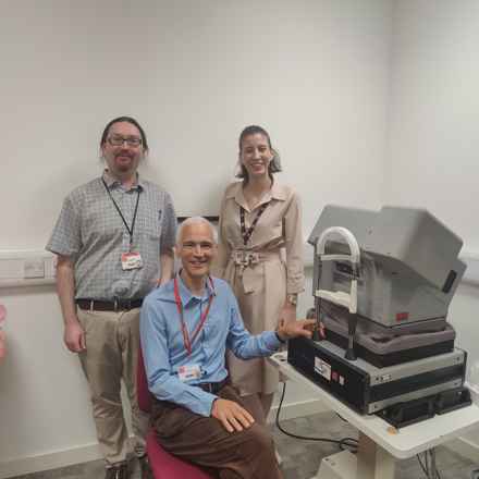 Image of the Cardiff research team, stood next to optometry equipment, a large eye scanner. 