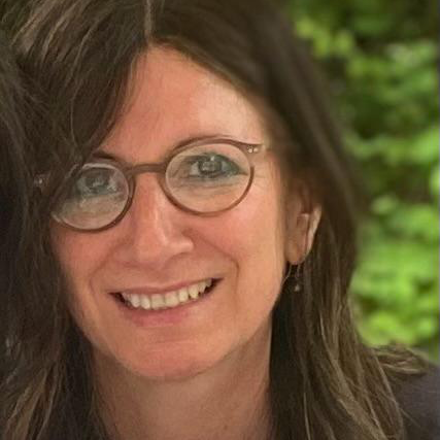 Elena Schiff. A white woman with long dark hair and glasses. She is smiling. 