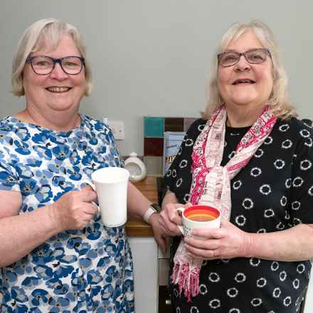 Friends Lynne, left, and Karen smile to the camera while holding cups of tea.