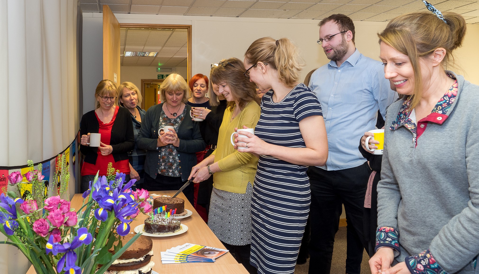 Staff smiling as they cut cake