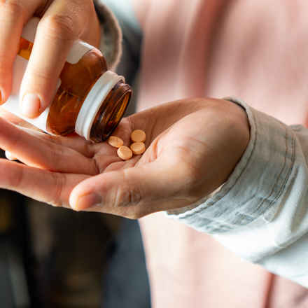 One hand holding a pill bottle tipping the pills out into an open hand, which holds two pills. 